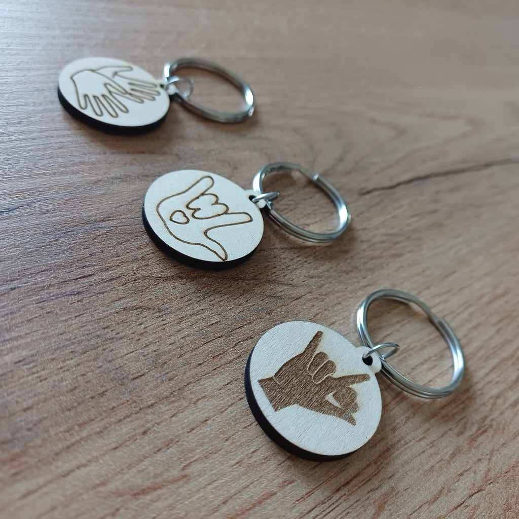 Trois mini porte-clés ronds en bois gravés en Langue des Signes LSF posés sur une table
