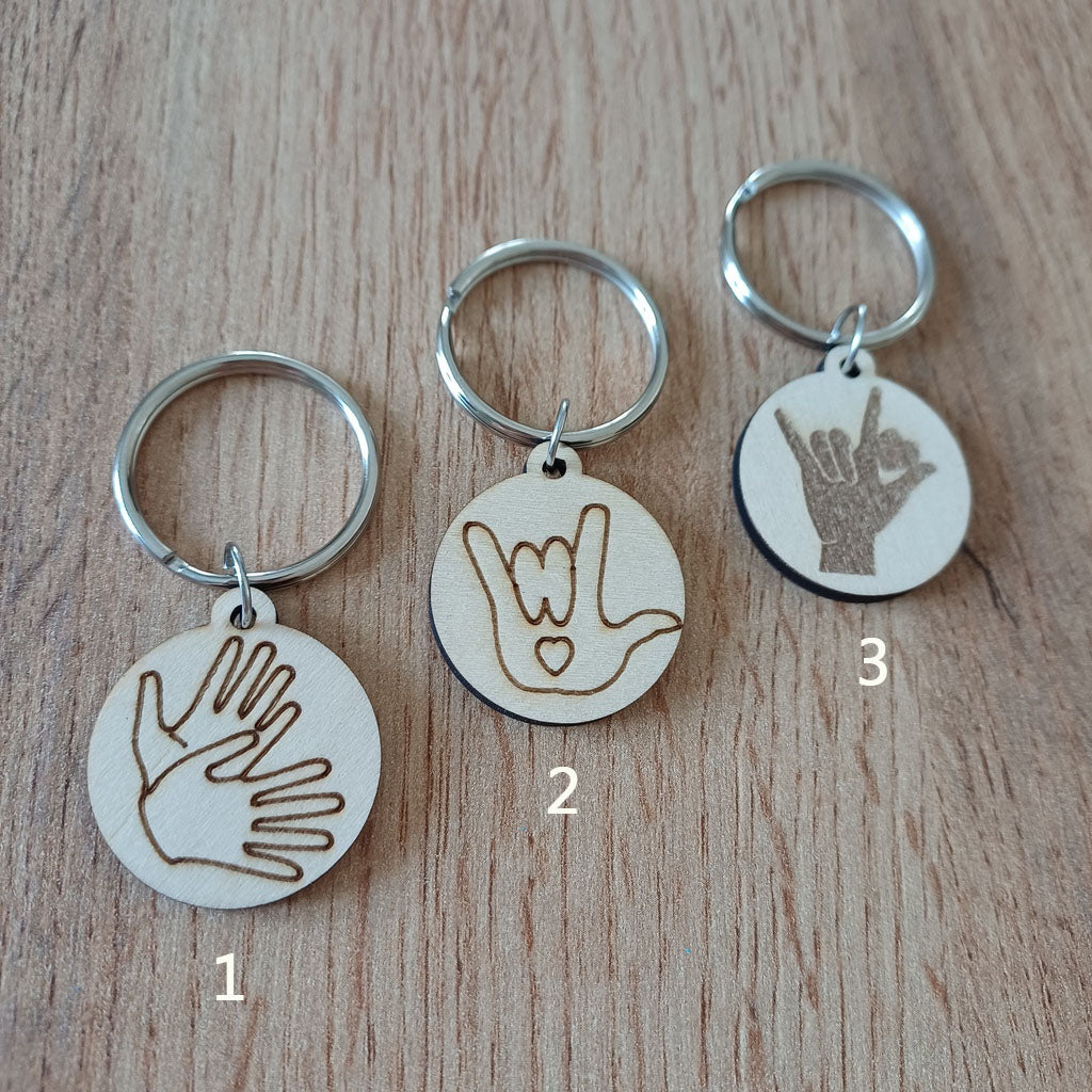 Trois mini porte-clés ronds en bois gravés en Langue des Signes LSF posés sur une table