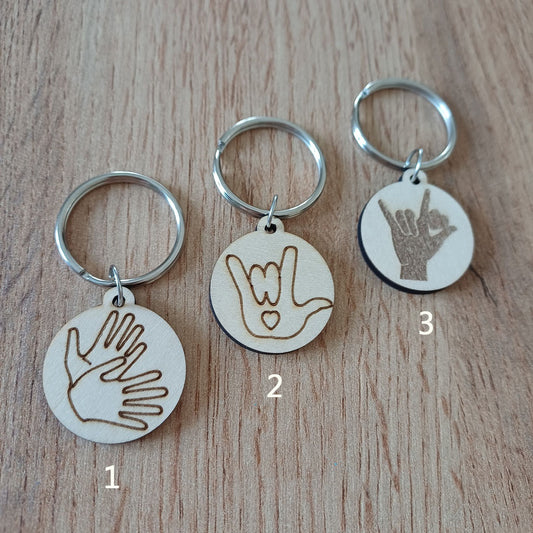 Trois mini porte-clés ronds en bois gravés en Langue des Signes LSF posés sur une table
