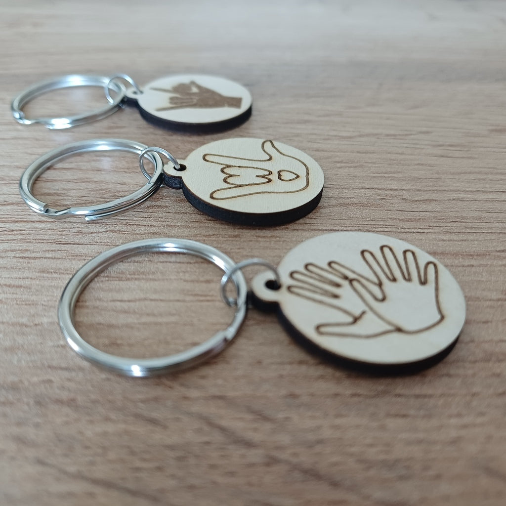 Trois mini porte-clés ronds en bois gravés en Langue des Signes LSF posés sur une table