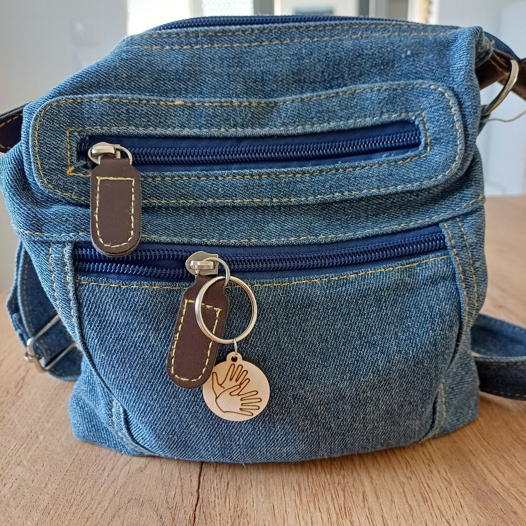 Mini porte-clés ronds en bois gravés du symbole SIGNER accroché sur un sac en jeans